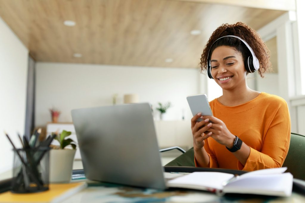 Smiling black woman in wireless headhones using cellphone